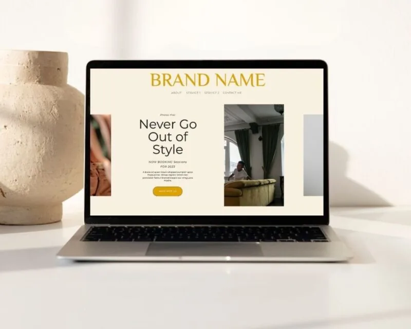A laptop displaying a minimalist Free Showit website template with a neutral background, bold yellow headline reading “Brand Name,” and a centered section with the text “Never Go Out of Style.” The layout includes images, navigation links, and a call-to-action button that says “Work With Us.”